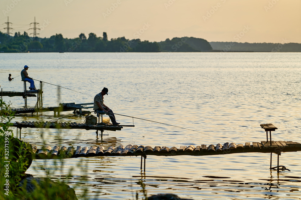 男性渔民拿着鱼竿坐在湖面或池塘上，从后面看。夏季钓鱼。
