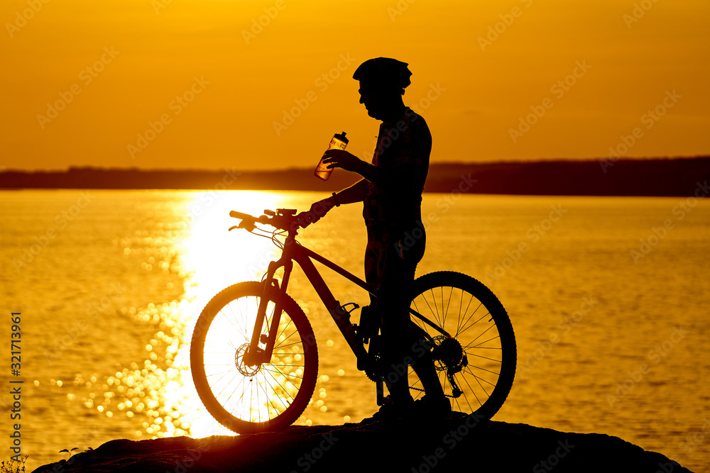 silhouette of a cyclist with sunset background. Orange sky, hobby, healthy habbits. Drinking water w