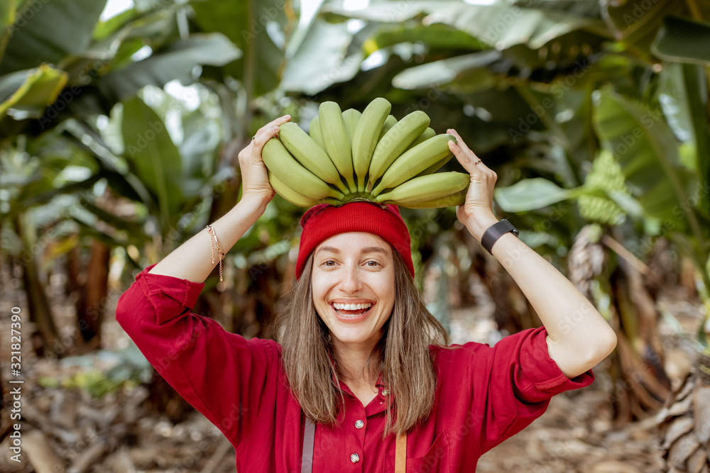 Portrait of a cute smiling woman holding a stem with fresh green bananas above the head. Healthy eat