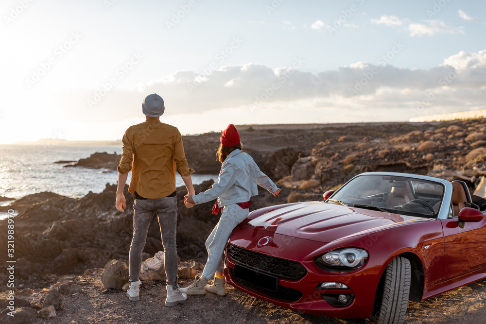 情侣们一起站在岩石海岸的汽车旁，欣赏着美丽的海景。汽车