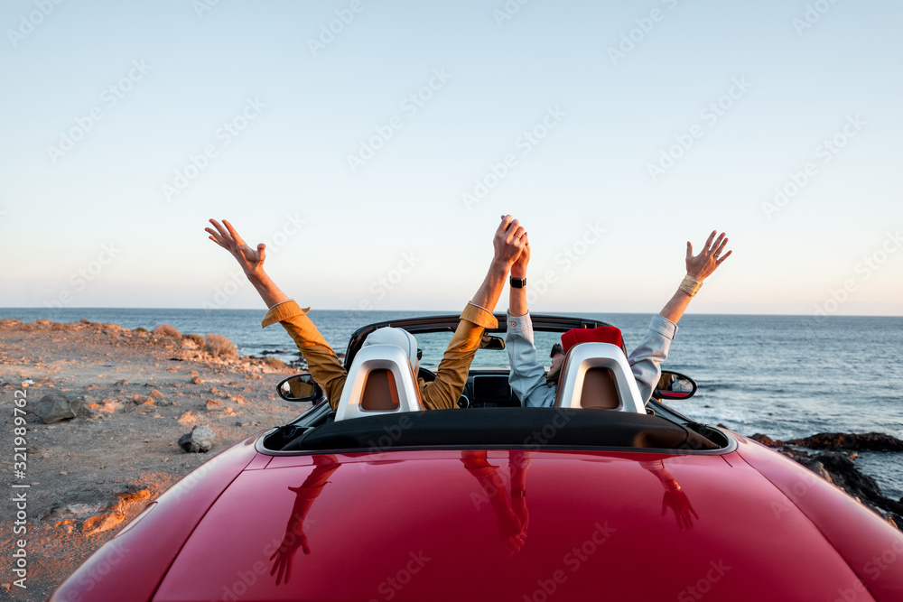 一对夫妇开着敞篷车，日落时在海边旅行，从背后看风景。快乐