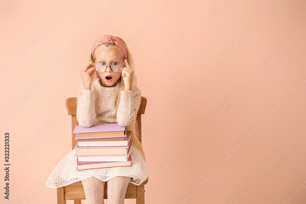 Surprised little girl with books on color background