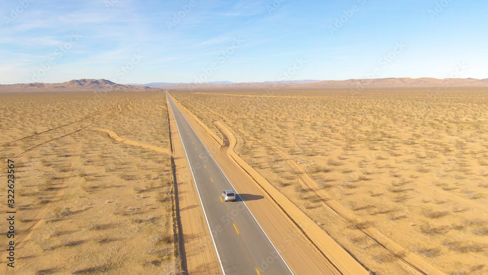无人机：一辆银色汽车在穿越沙漠的高速公路上行驶时，在后面飞行