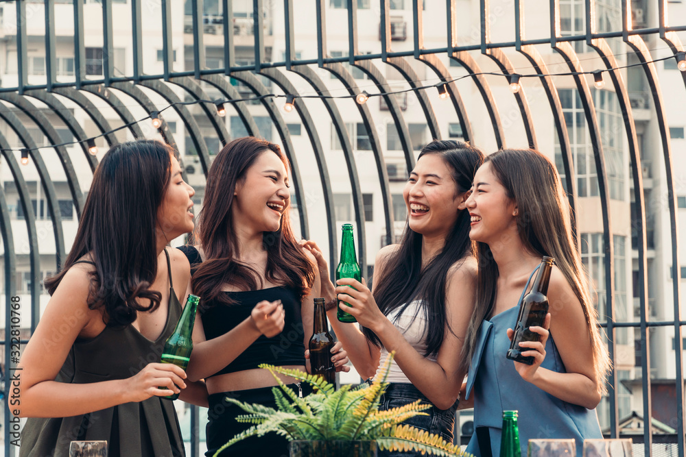 Group of happy Asian girl friends celebrating party with beer bottle toasting drinks at rooftop cafe