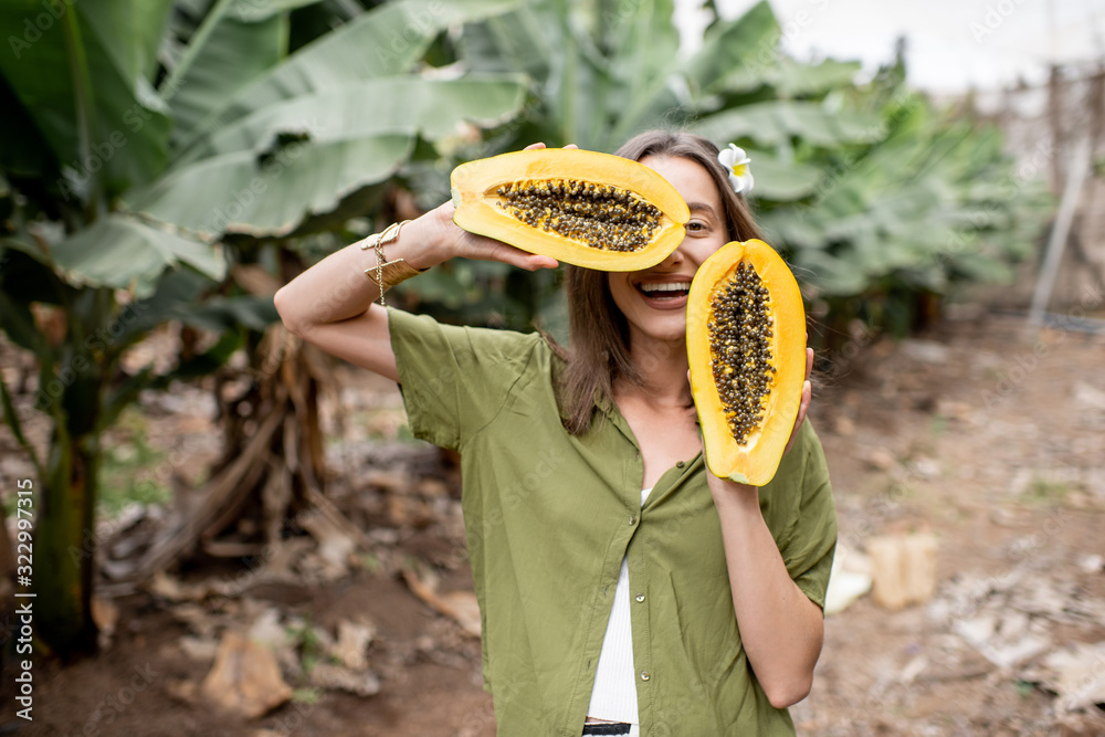 Portrait of a young woman with sliced papaya fruit on the plantation. Concept of vegetarianism, heal
