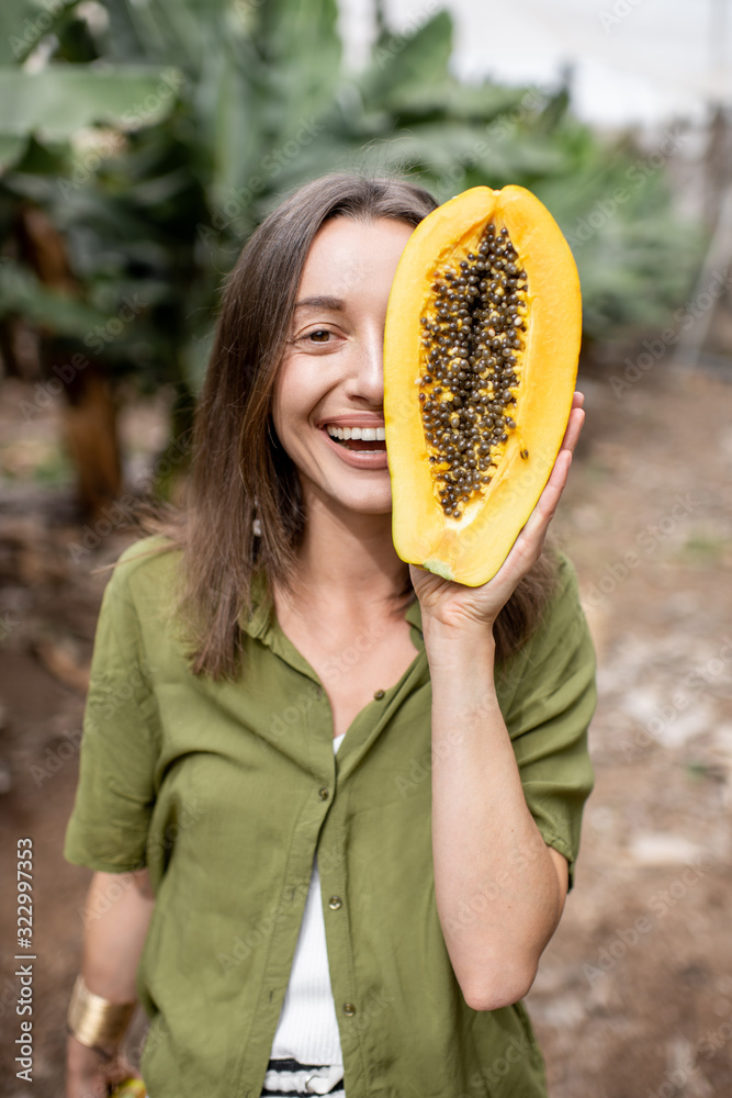 Closeup portrait of a young woman hiding her face behind sliced papaya fruit outdoors on the green b
