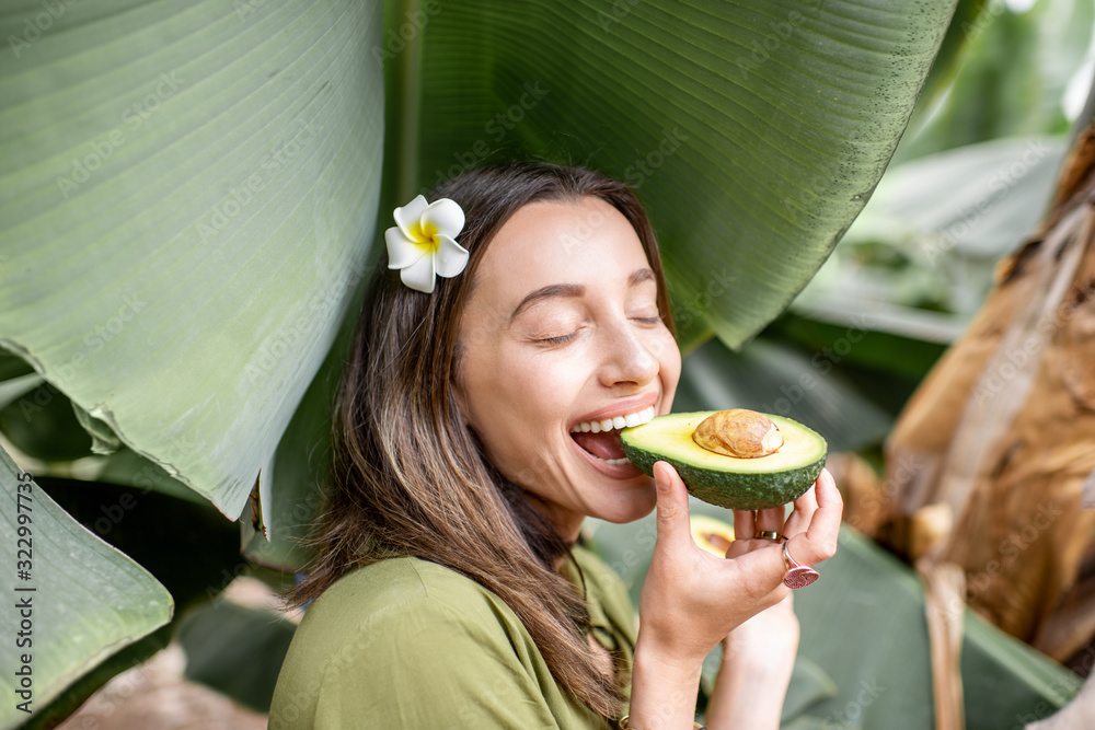 年轻女子在户外香蕉叶中吃鳄梨浆果。素食主义的概念，健康的ea