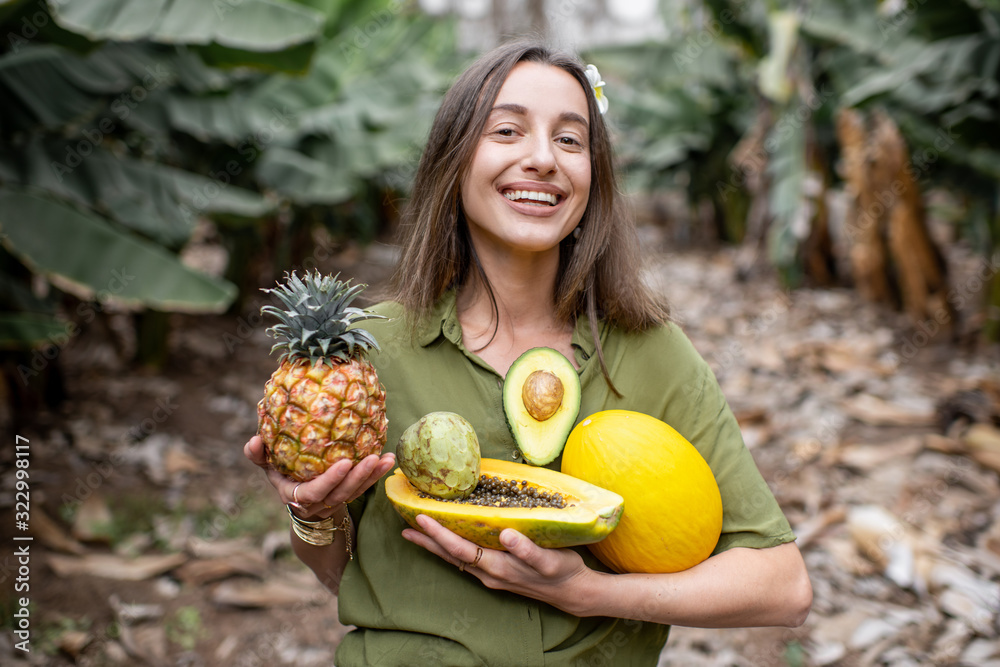 一个年轻微笑的女人的画像，她在户外吃着异国情调的食物，手里拿着ananas、木瓜、甜瓜、鳄梨