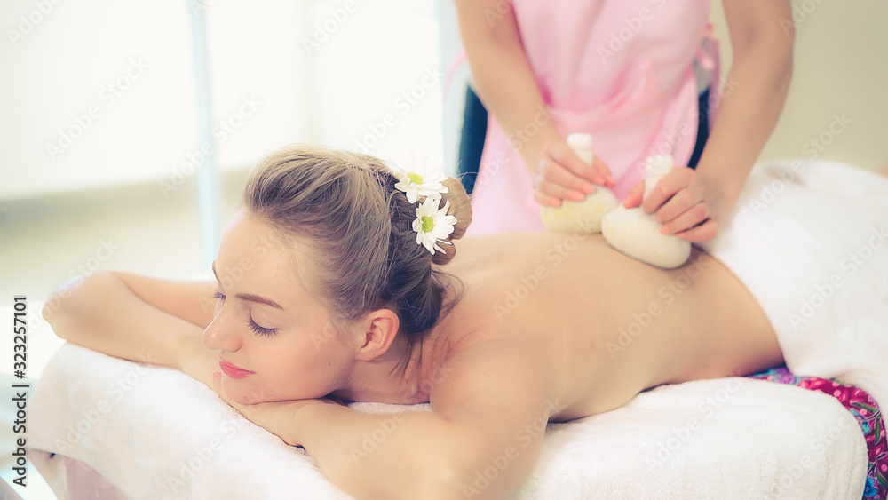 Massage therapist holds a herbal compress to do treatment to woman lying on spa bed in a luxury spa 