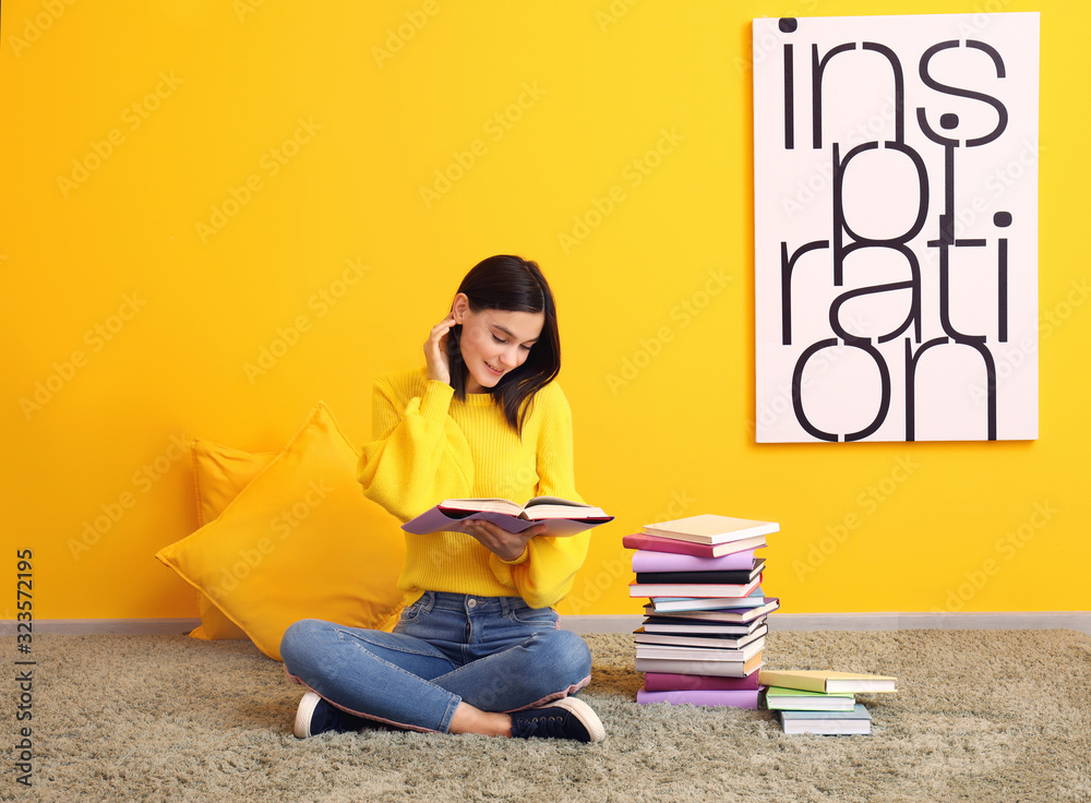 美丽的年轻女子在彩色墙附近拿着书