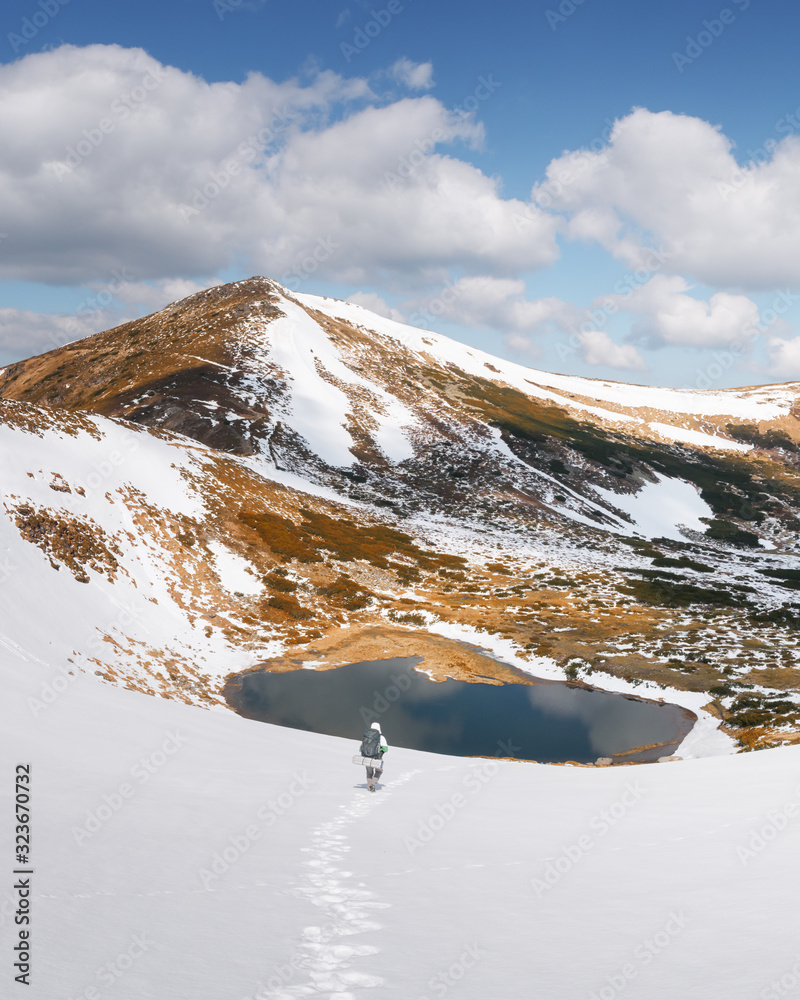 Amazing landscape with lake in spring snowy mountains. Hiker with backpack coming down in the snow