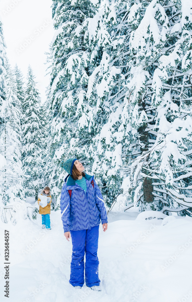 Mother and son have a winter snowy forest walking. Woman standing on the path, rising head up and en