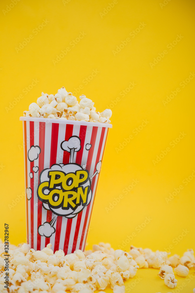 红色爆米花杯里的黄油爆米花，黄色背景下的房子或电影院里的零食