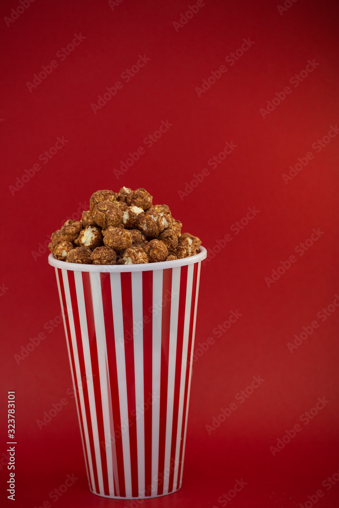 Butter popcorn in a red popcorn cup, snack in the house or cinema on a red background