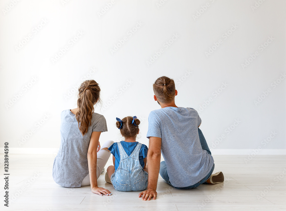 happy family mother, father and child daughter   backs on blank grey wall