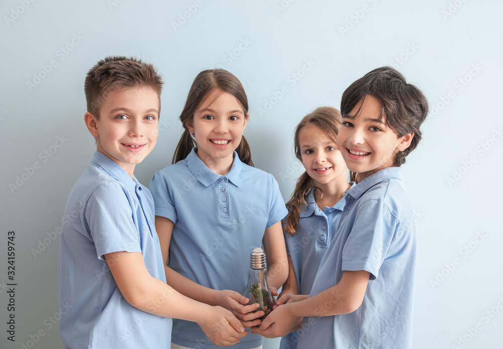 Little children holding light bulb with plant on color background. Earth Day celebration