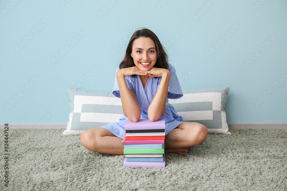 Beautiful young woman with books near color wall