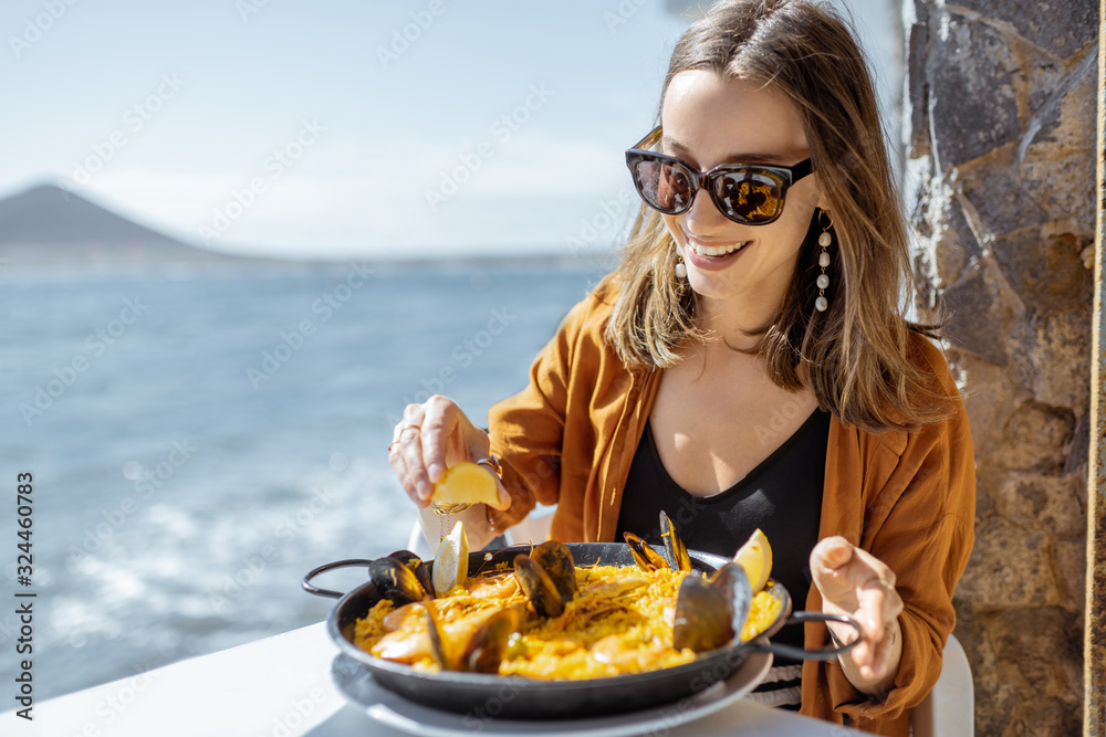 女人坐在餐厅露台上吃西班牙传统菜肴海鲜饭