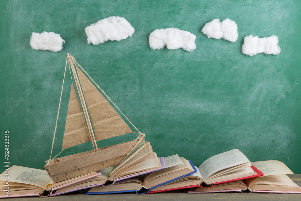 教育是一个旅程概念，玩具船和书籍就像黑板背景上的海浪，在