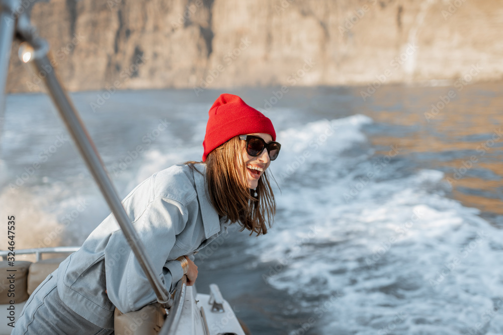 一位年轻女性旅行者的肖像，她戴着红帽子，穿着牛仔裤，在附近的游艇上航行