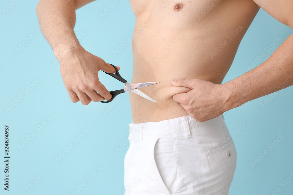 年轻人拿着剪刀在彩色背景上触摸腹部脂肪。整形手术概念