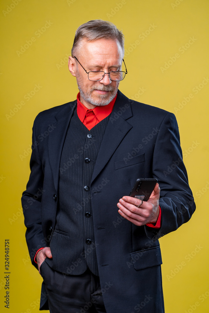 一位资深商人手持手机，站在工作室的黄色背景下的肖像