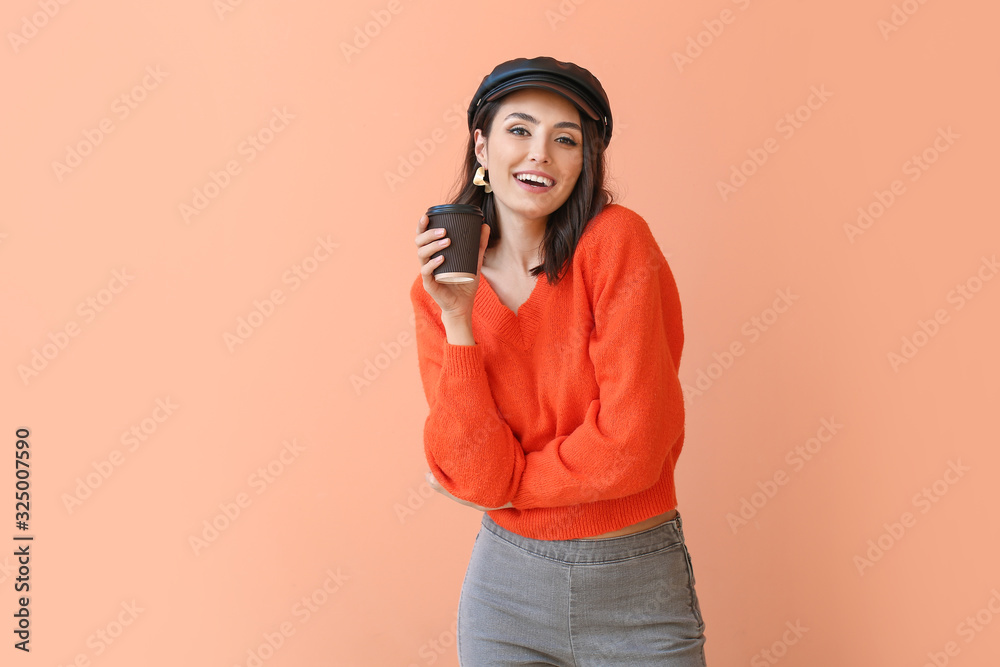 穿着保暖毛衣的漂亮年轻女子在彩色背景下喝咖啡