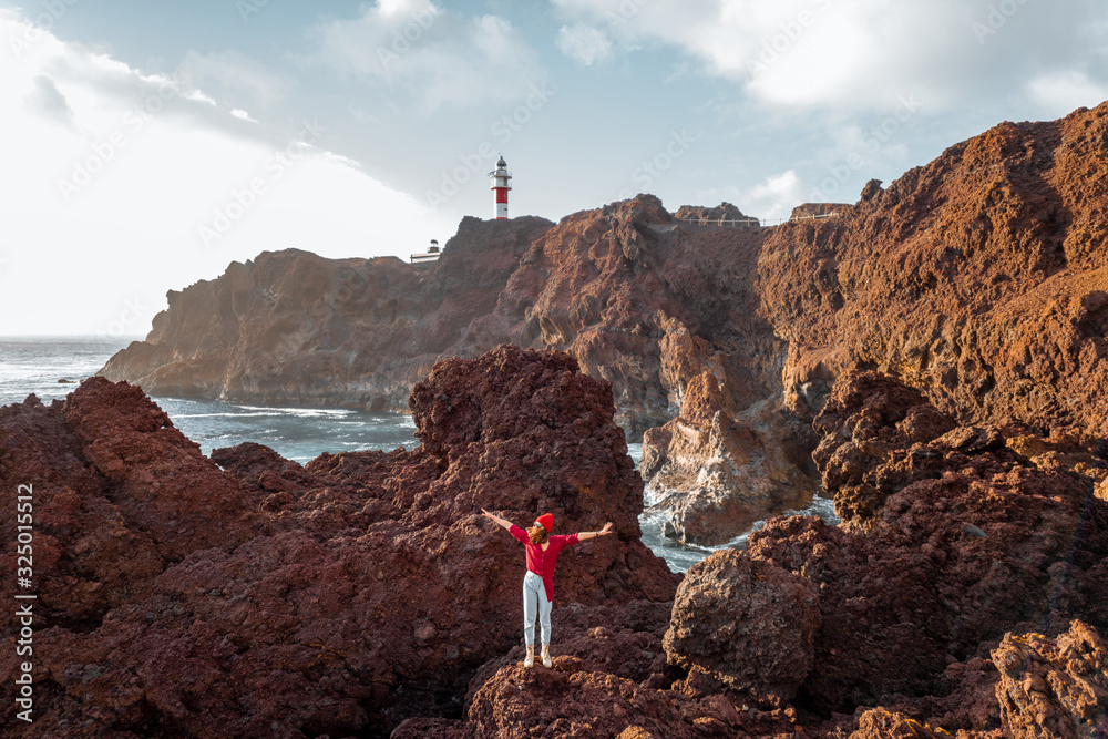 Woman enjoying great views on the rocky ocean coast and a lighthouse on the background, traveling on