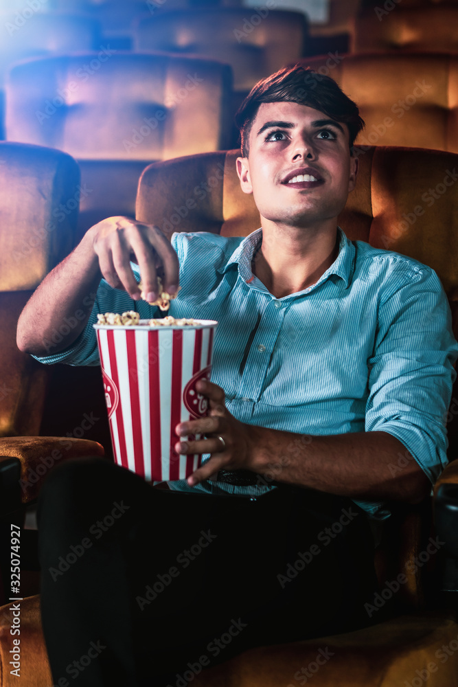 一个年轻人在电影院看电影时笑着拿着爆米花