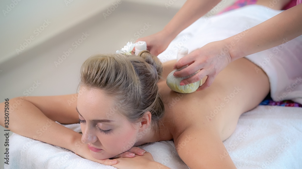 Massage therapist holds a herbal compress to do treatment to woman lying on spa bed in a luxury spa 
