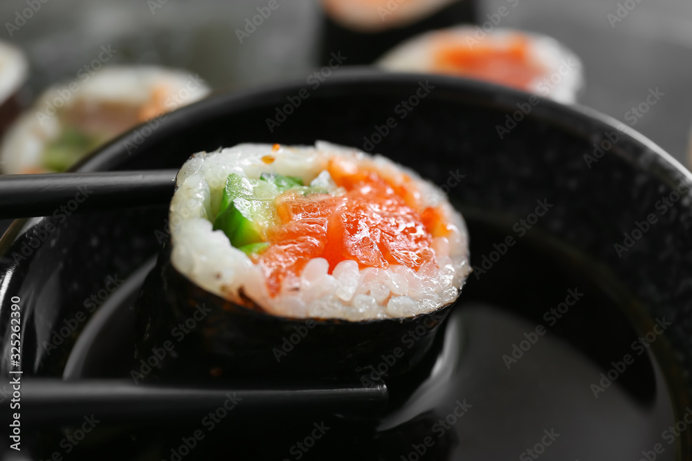 Dipping of tasty sushi roll into soy sauce, closeup