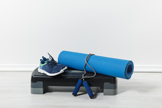 step platform, fitness mat, jump rope and sport shoes on floor at home