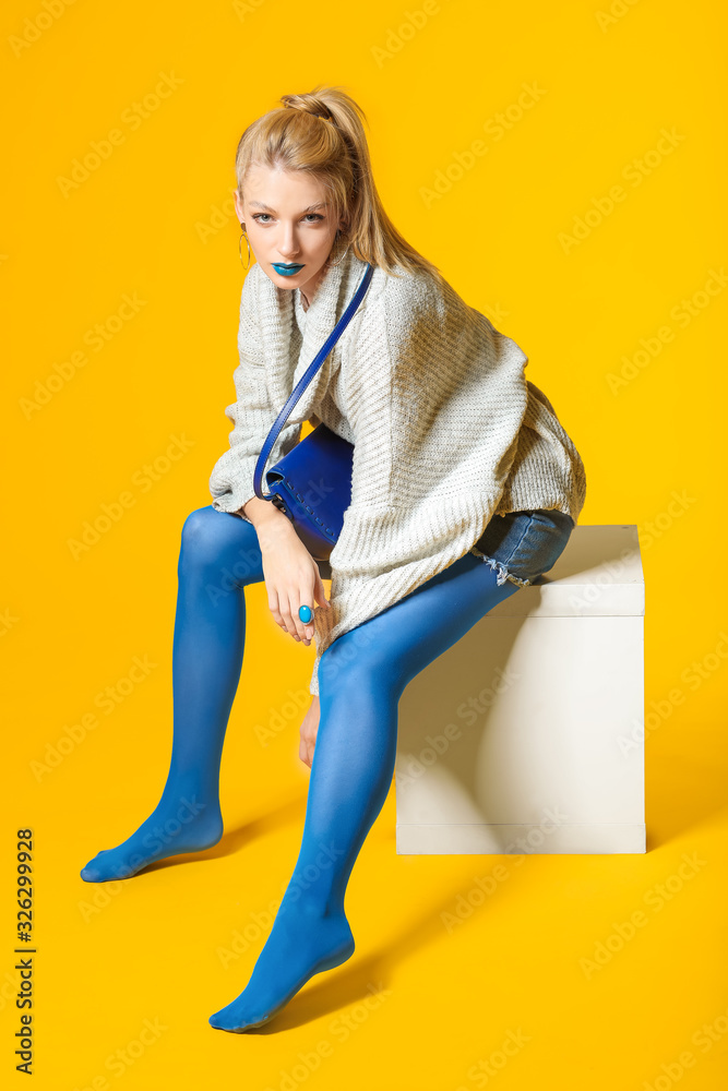 年轻女性，化着富有创意的妆，穿着彩色背景的保暖毛衣