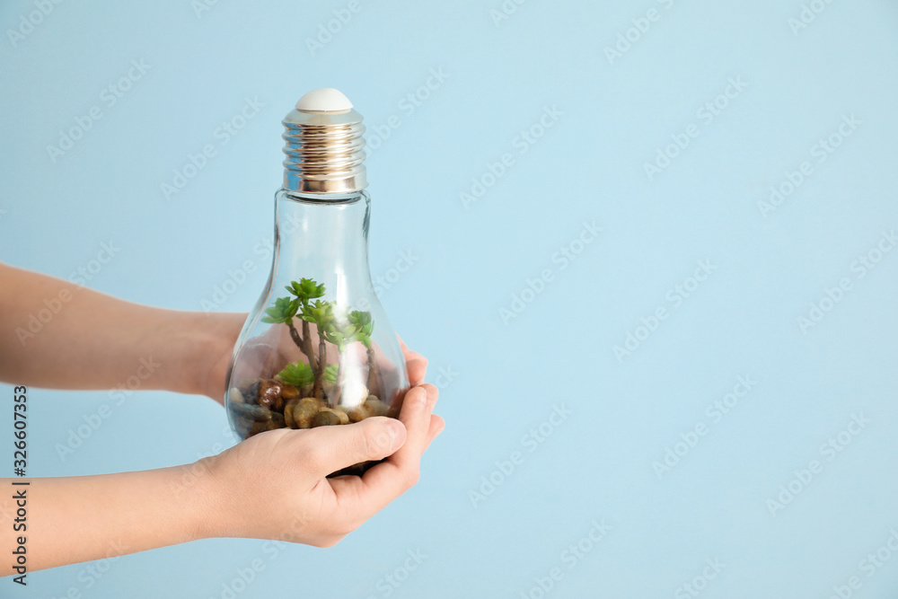 Little child holding light bulb with plant on color background. Earth Day celebration