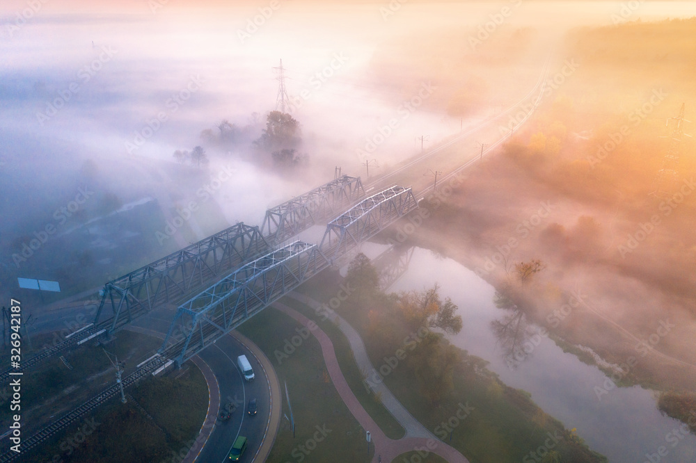 Aerial view of beautiful railroad bridge and river in fog at sunrise in fall. Autumn landscape with 