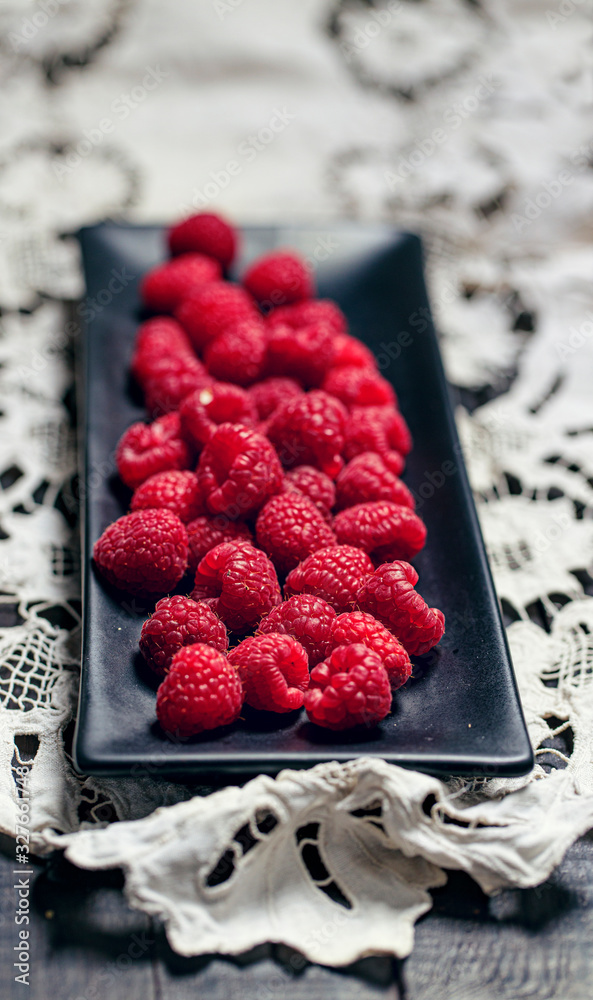 Front view on ripe raspberries in black rectangular plate on white handymade napkin