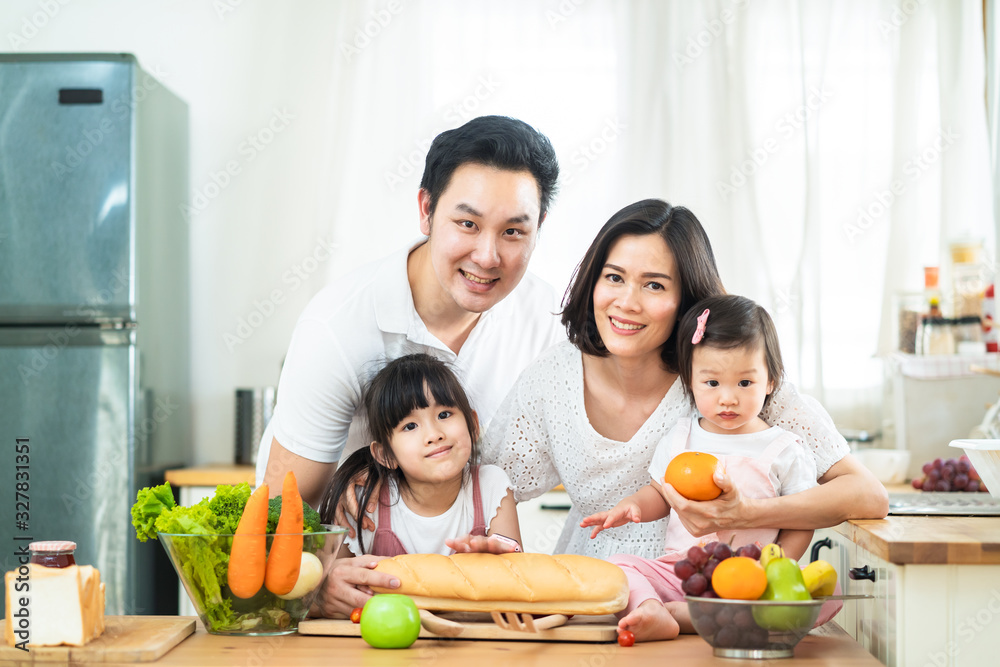 可爱可爱的亚洲家庭在家里的厨房里做食物。微笑的母亲、父亲和孩子的肖像
