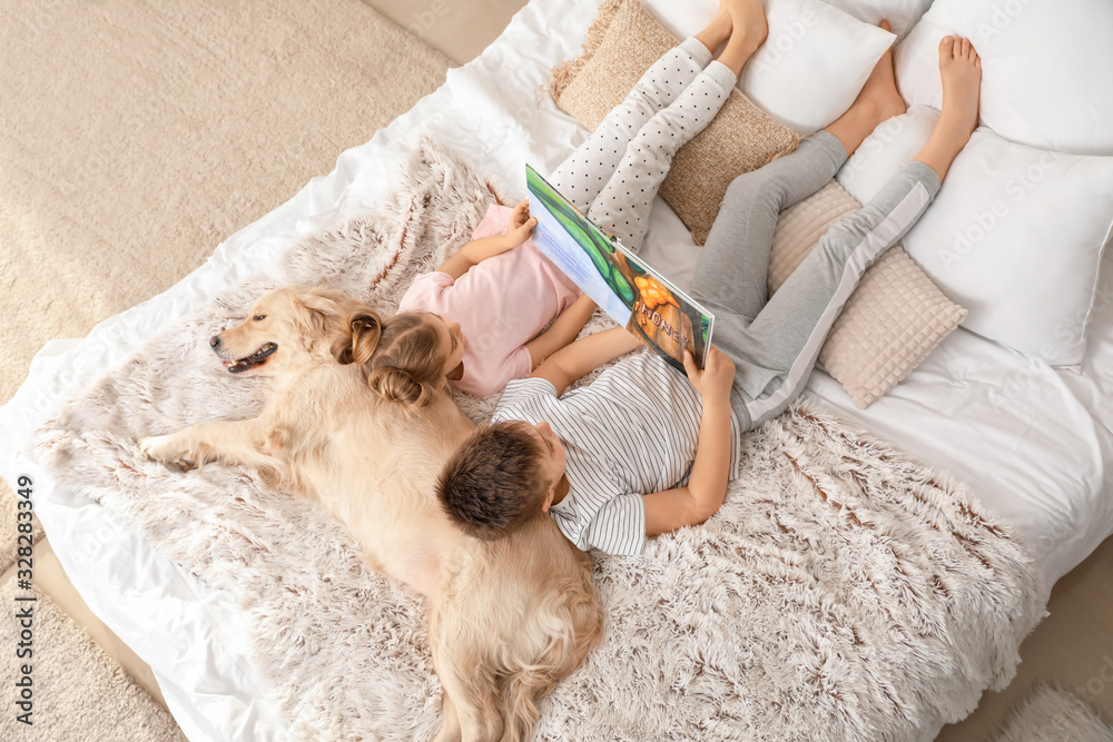 Little children with dog reading book in bedroom at home