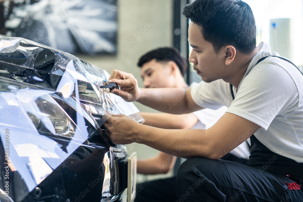 两名亚洲汽车贴膜保护男工人在车库为黑色汽车安装贴膜。男子关注ho