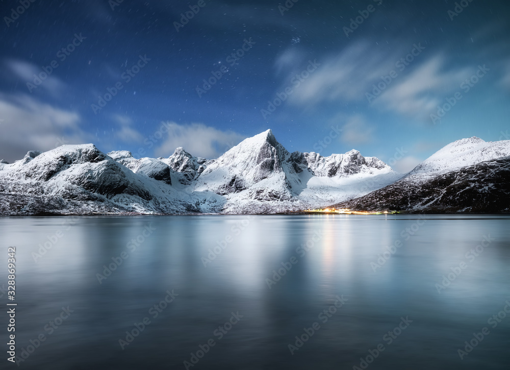 Mountains and reflections on water at night. Winter landscape. The sky with stars and clouds in moti