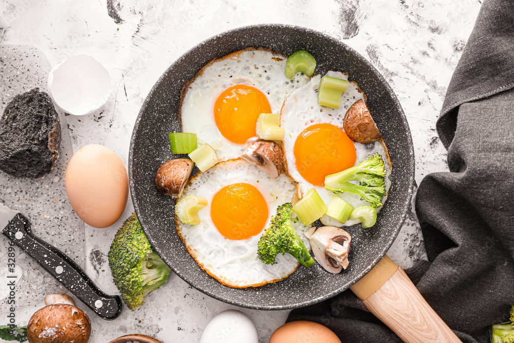 Frying pan with cooked eggs and vegetables on white background