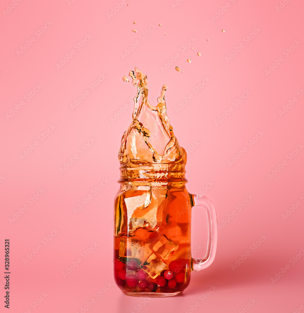 Mason jar of cold tea with splashes on color background