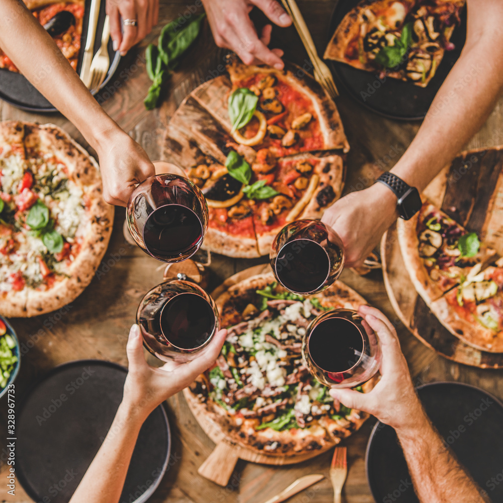 Family or friends having pizza party dinner. Flat-lay of people clinking glasses with red wine over 