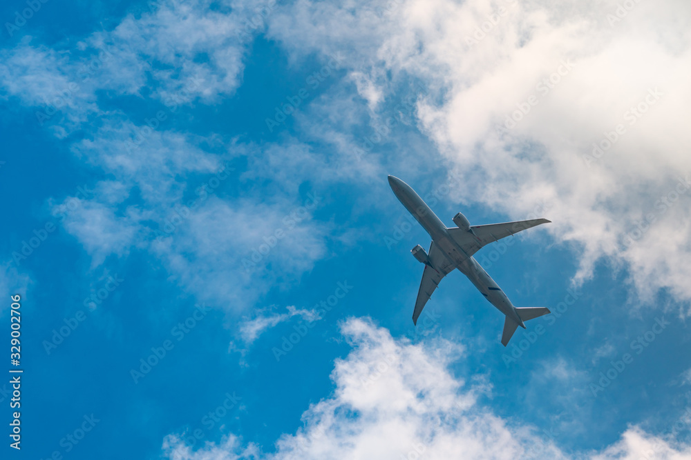 Commercial airline flying on blue sky and white fluffy clouds. Under view of airplane flying. Passen