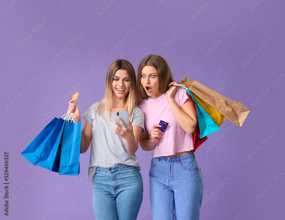 Young women with mobile phone and shopping bags on color background