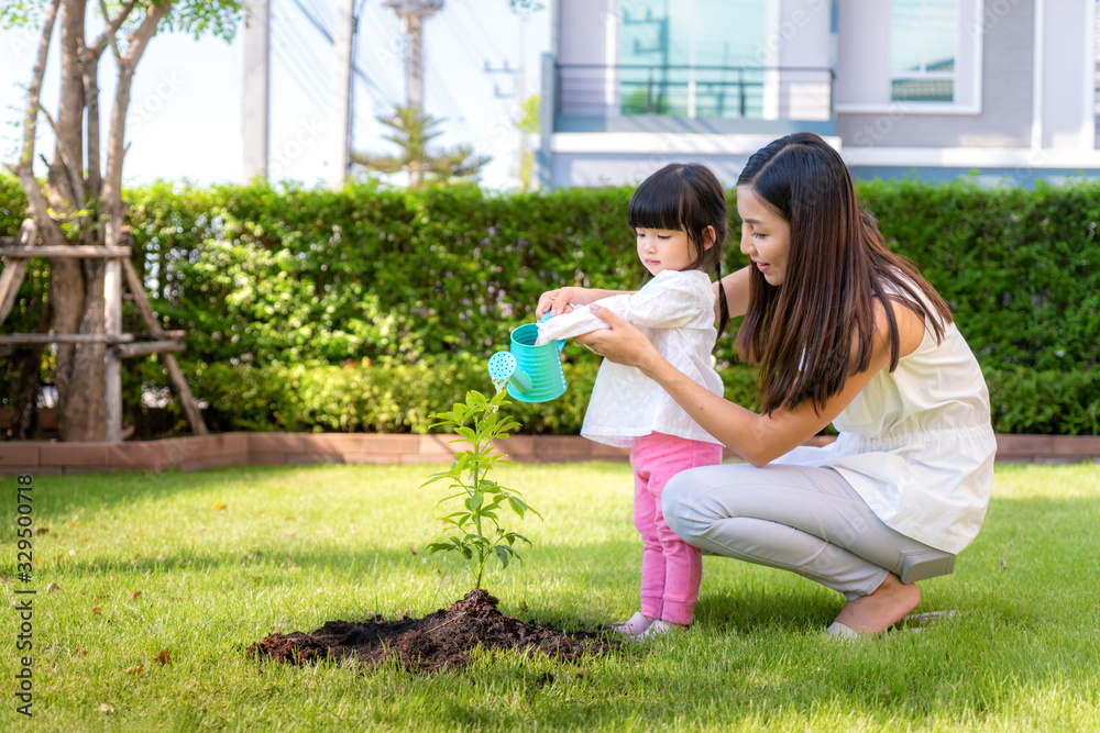 Asian family mother and kid daughter plant sapling tree and watering outdoors in nature spring for r