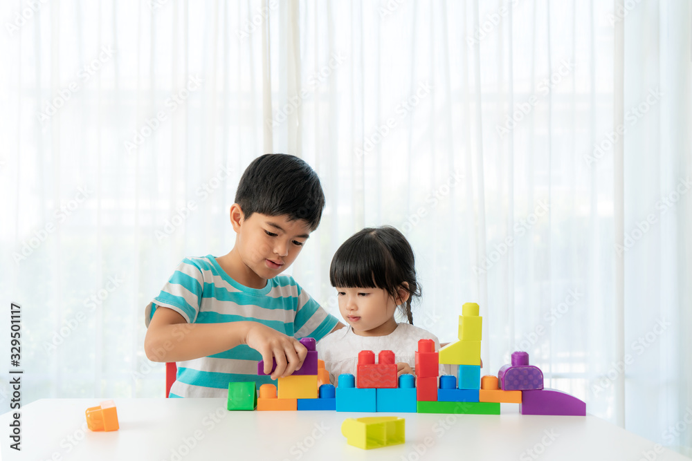 亚洲可爱的兄弟姐妹在家里客厅的桌子上与玩具积木设计师玩耍。Co