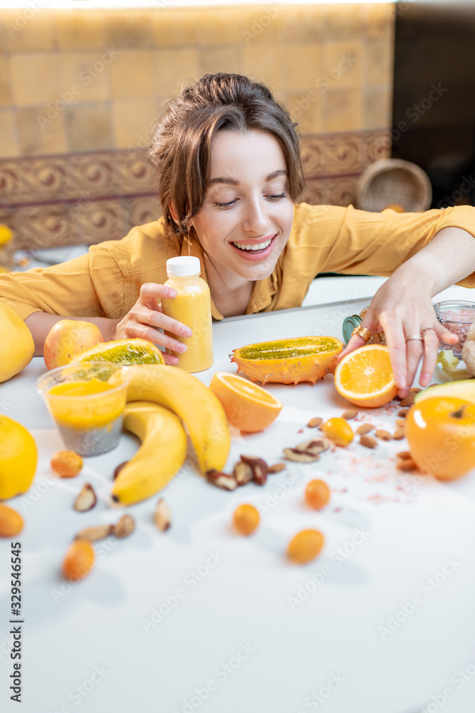 一个年轻快乐的女人拿着一瓶果汁坐在装满健康生蔬菜的桌子旁的肖像