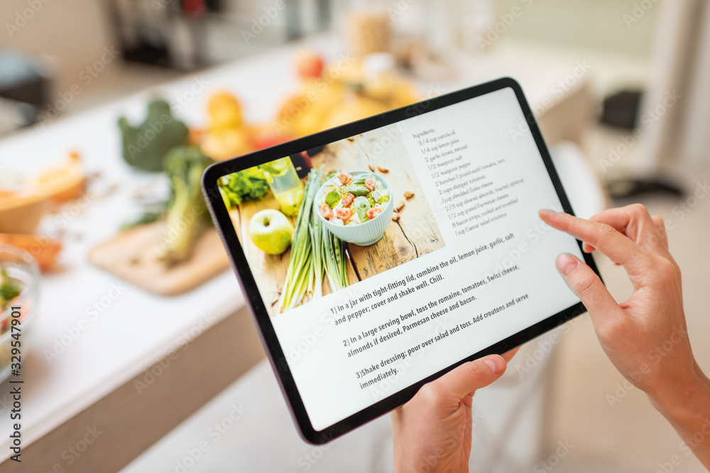 Woman looking on the digital recipe, using touchscreen tablet while cooking healthy meal on the kitc