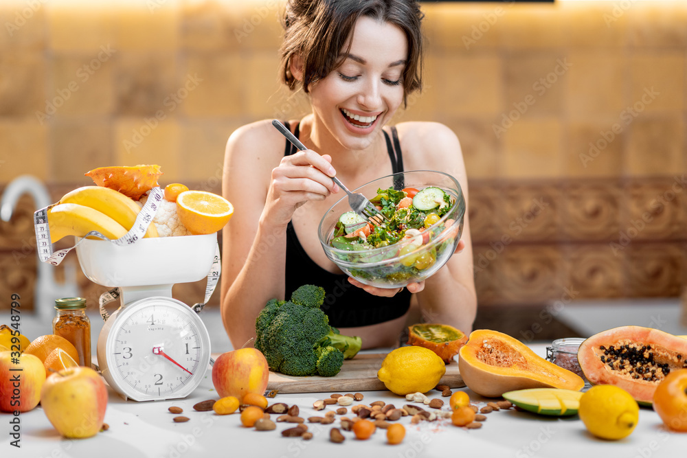 运动女性吃沙拉，站在厨房里吃很多健康的新鲜食物。losin的概念